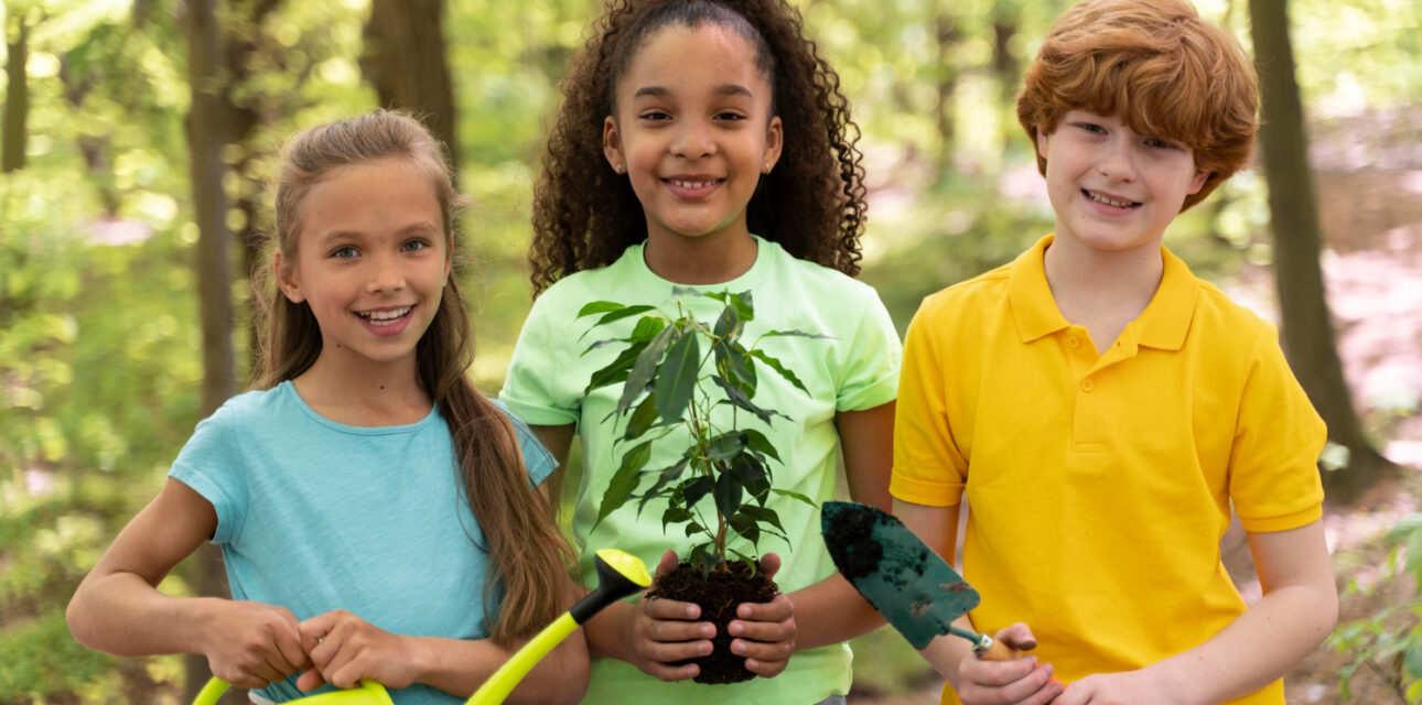 Three autistic children in Colorado holding gardening tools and a small plant in a forest.