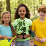 Three autistic children in Colorado holding gardening tools and a small plant in a forest.
