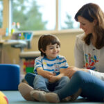 BCBA sitting on the floor, smiling and interacting with a child during ABA therapy session.