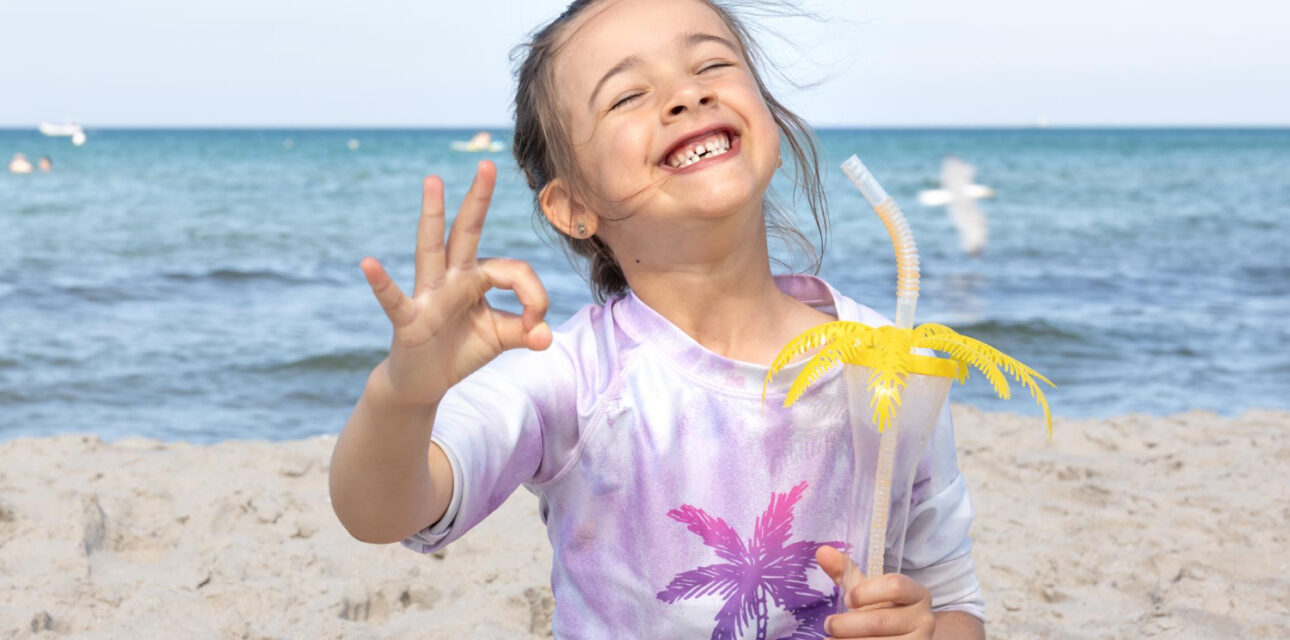 Smiling child on a beach holding a drink.