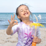 Smiling child on a beach holding a drink.
