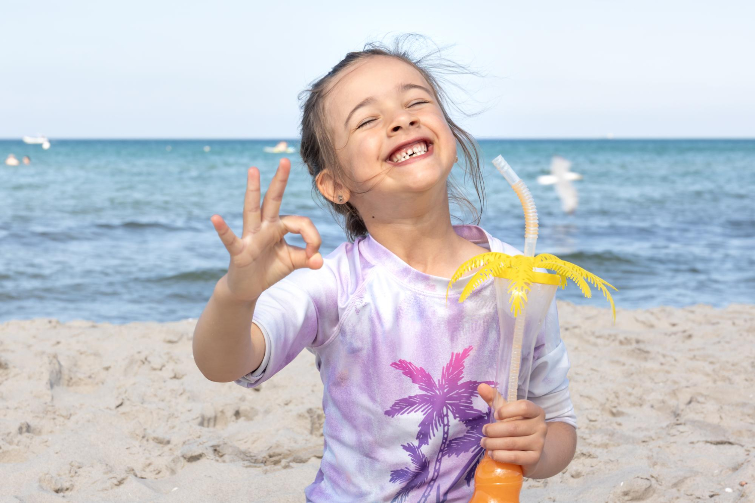 Smiling child on a beach holding a drink.