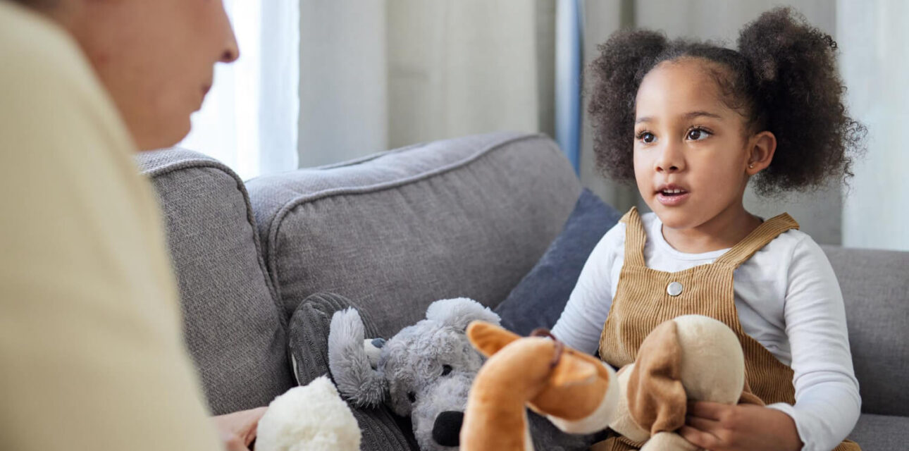 Young child talking with an ABA therapist while holding stuffed animals during ABA therapy.