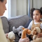 Young child talking with an ABA therapist while holding stuffed animals during ABA therapy.