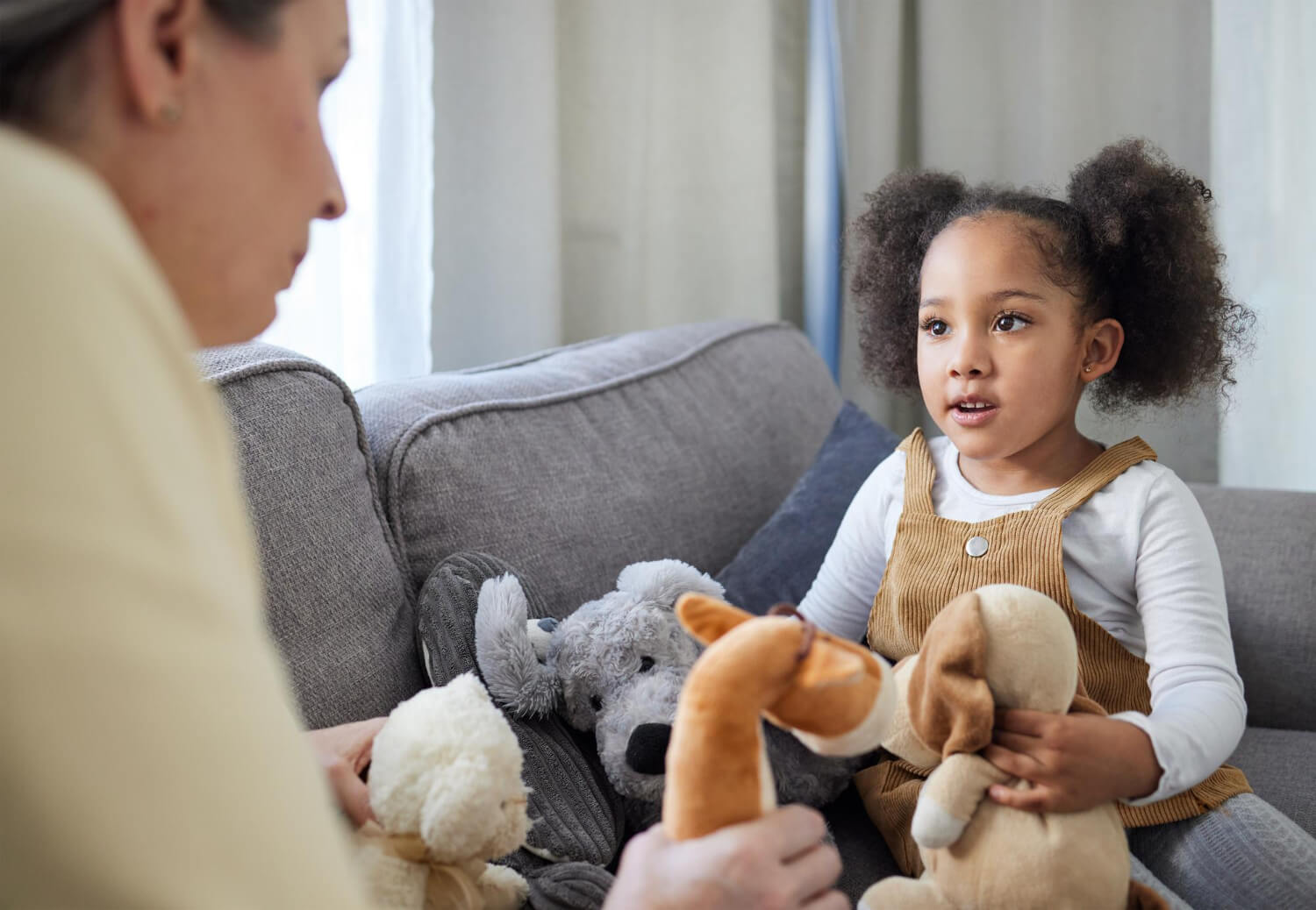 Young child talking with an ABA therapist while holding stuffed animals during ABA therapy.