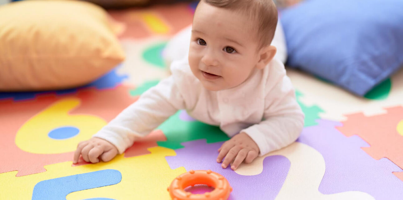 Baby crawling on a colorful foam play mat with a toy ring nearby during ABA therapy.