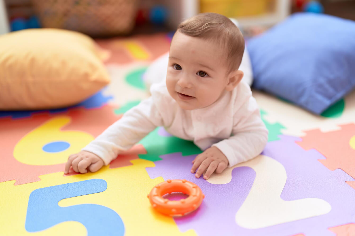 Baby crawling on a colorful foam play mat with a toy ring nearby during ABA therapy.