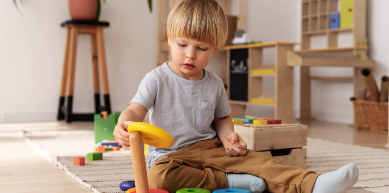 Toddler playing with a stacking ring toy on the floor during ABA therapy.