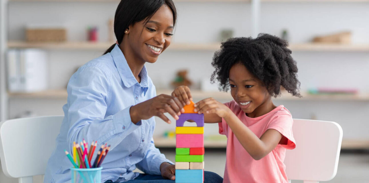 BCBA and child building a colorful block tower together at a table during ABA therapy.