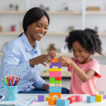 BCBA and child building a colorful block tower together at a table during ABA therapy.
