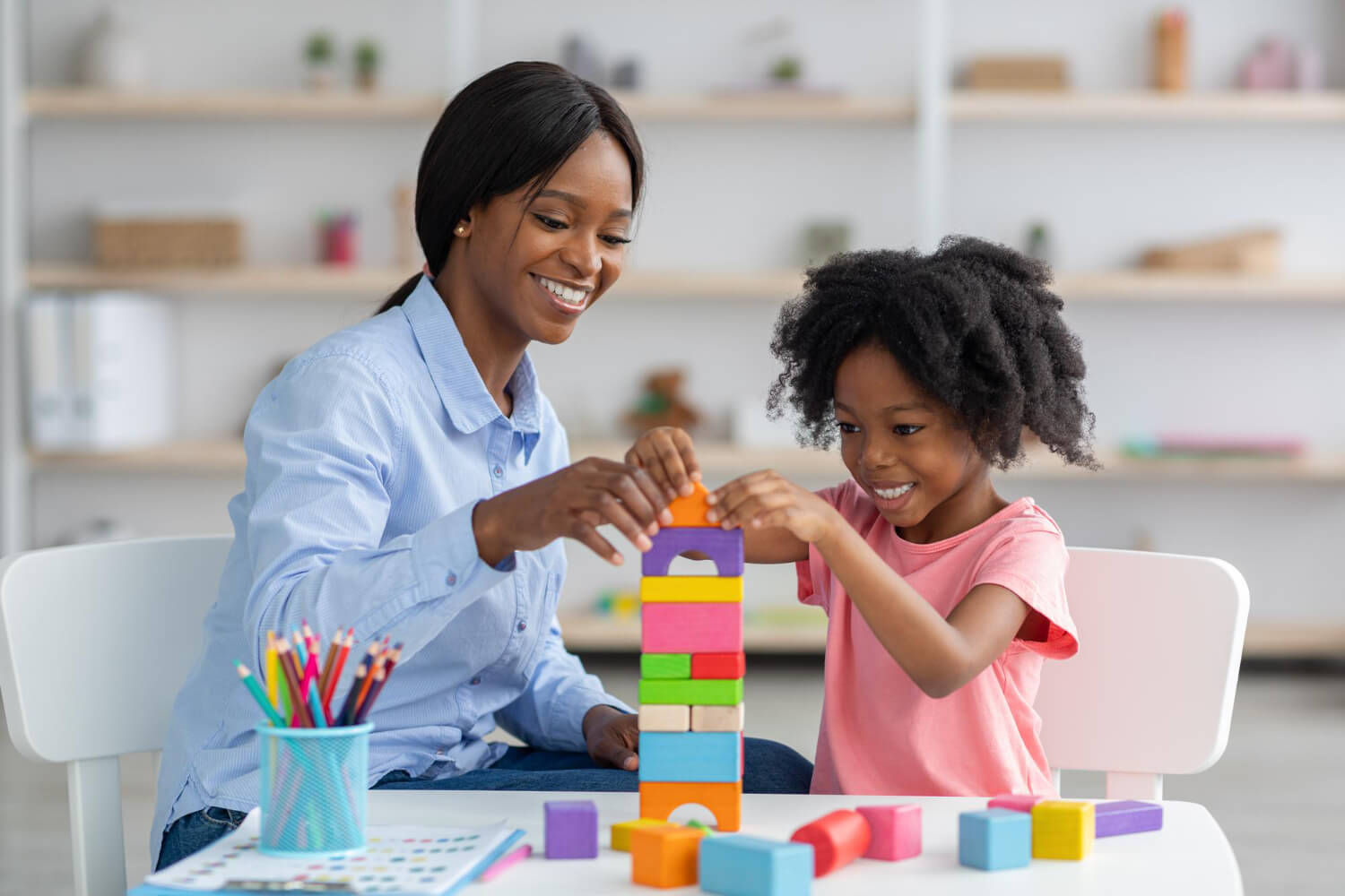BCBA and child building a colorful block tower together at a table during ABA therapy.