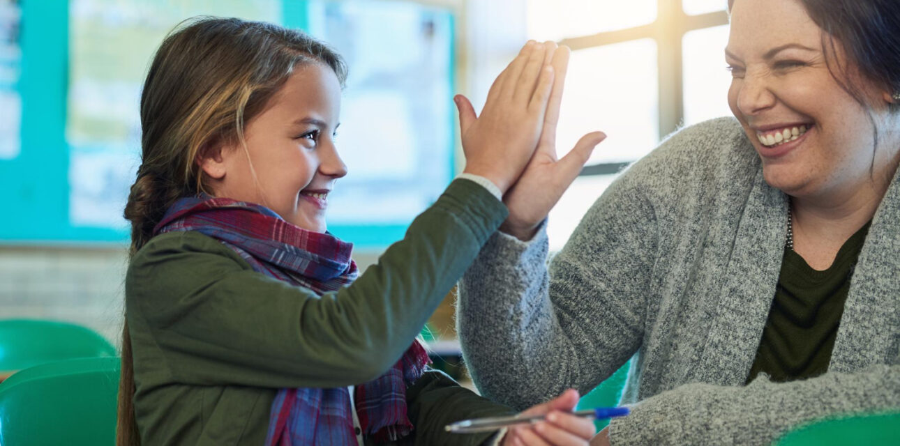 A smiling child and BCBA high-five in an ABA therapy center.