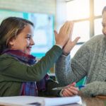 A smiling child and BCBA high-five in an ABA therapy center.