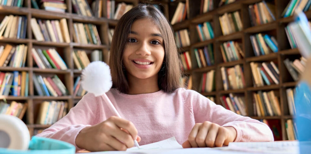 Autistic child smiling while writing at a desk in a library.