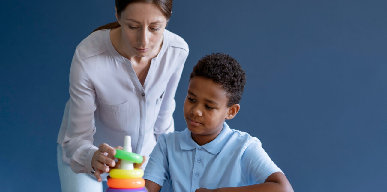 ABA therapist helping a young boy with stack colorful rings during therapy session.