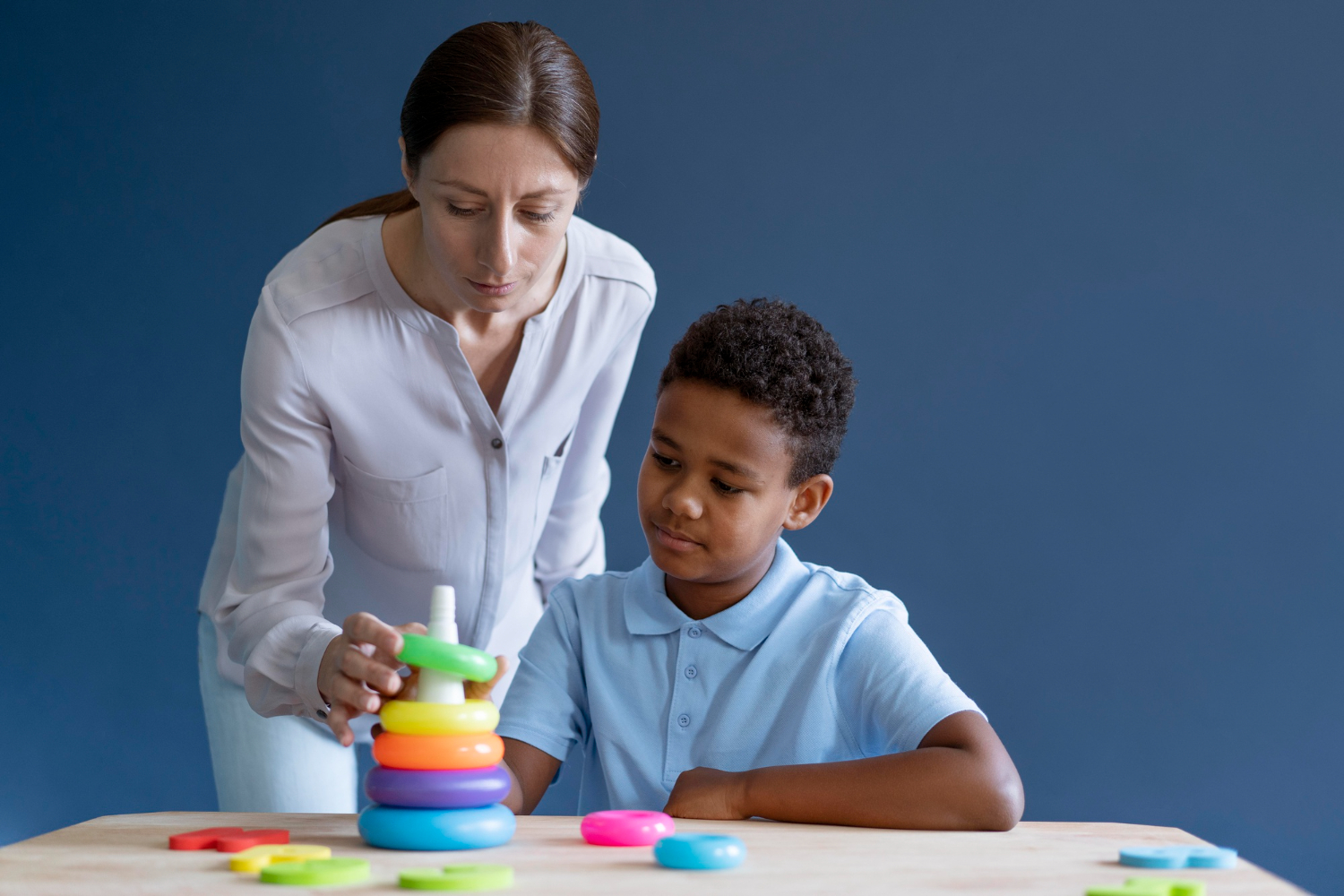 ABA therapist helping a young boy with stack colorful rings during therapy session.