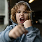 Autistic child showing frustration with clenched fists and open mouth.