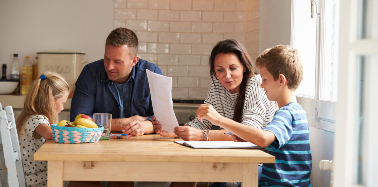 Parents help their two autistic children with homework while sitting together at a kitchen table.