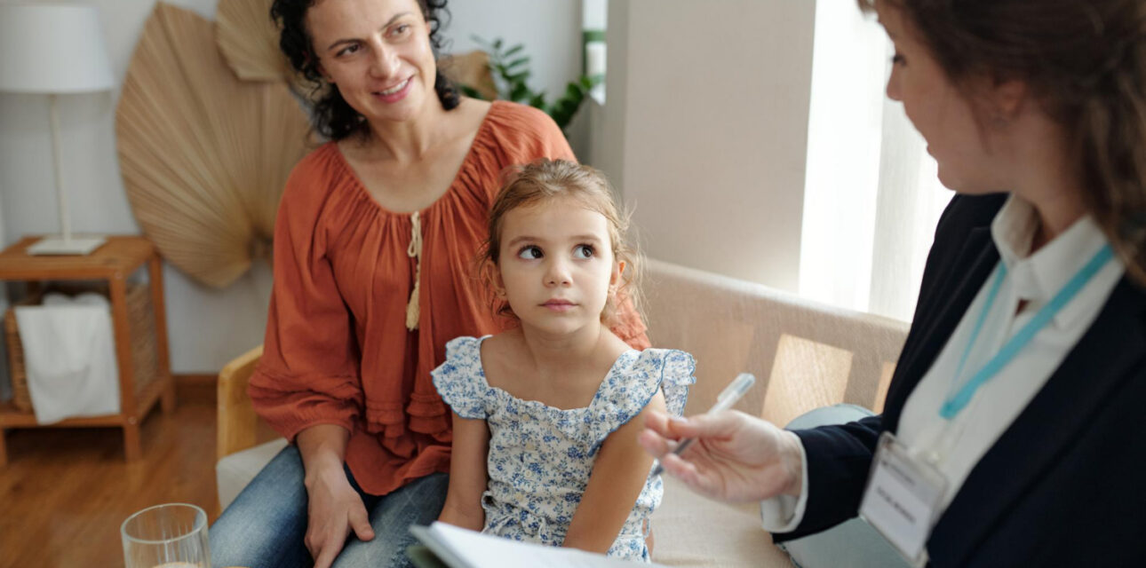 A young child and caregiver meet with an ABA therapist during an ABA therapy session in a comfortable office.