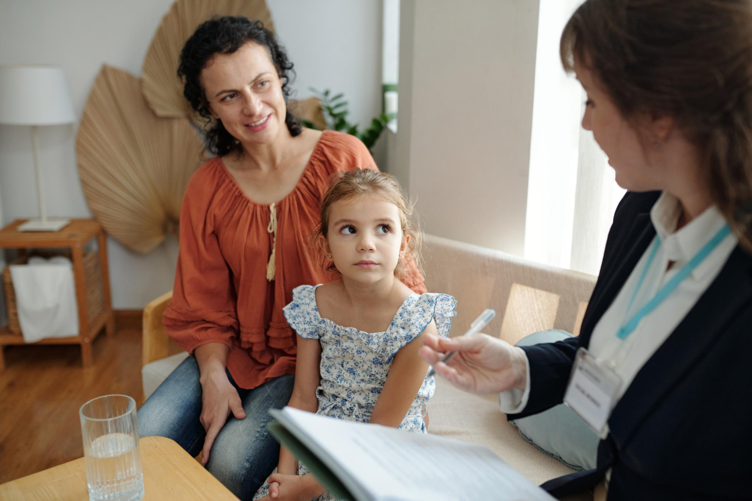 A young child and caregiver meet with an ABA therapist during an ABA therapy session in a comfortable office.