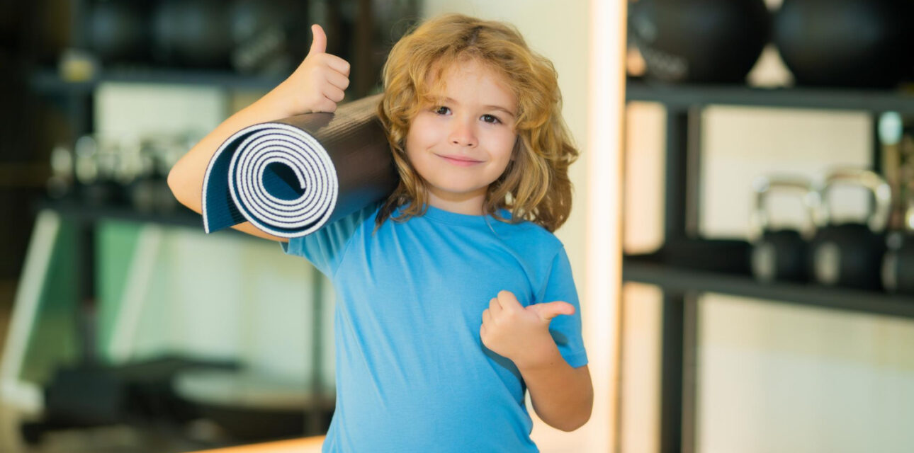 Autistic child holding a yoga mat and giving a thumbs-up.