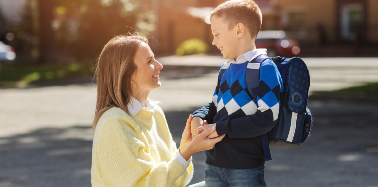 BCBA smiling with autistic boy wearing a backpack outdoors.