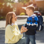 BCBA smiling with autistic boy wearing a backpack outdoors.