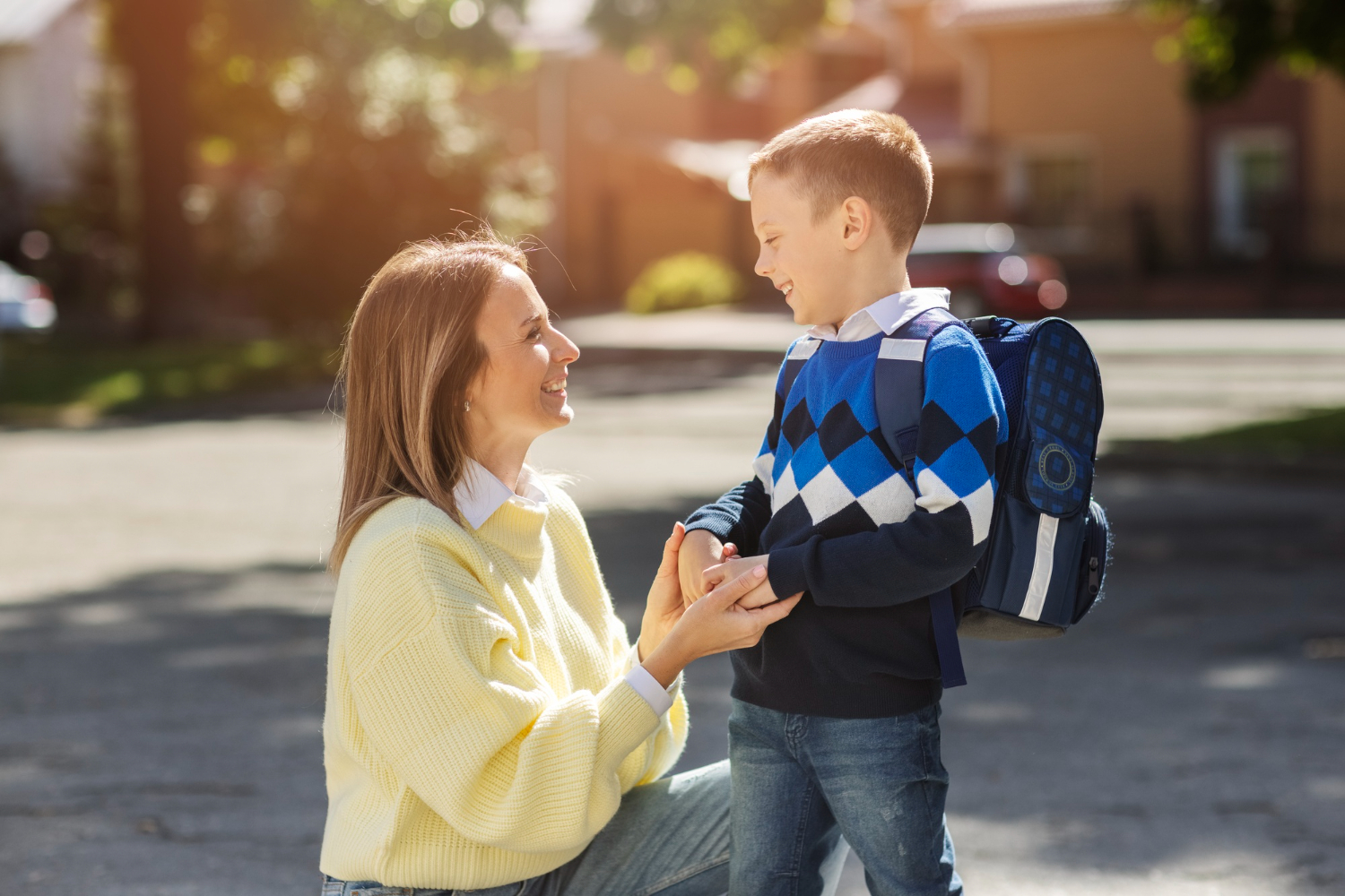 BCBA smiling with autistic boy wearing a backpack outdoors.