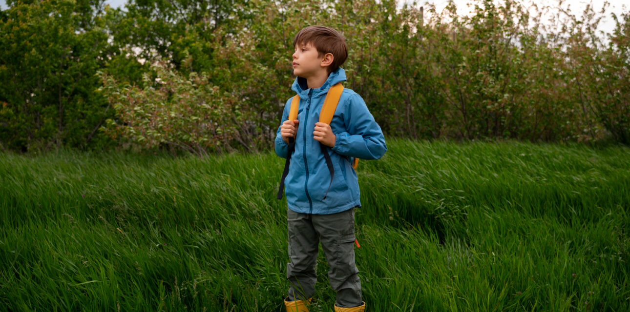Autistic child with a backpack standing in tall grass, looking into the distance.