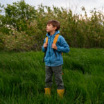Autistic child with a backpack standing in tall grass, looking into the distance.