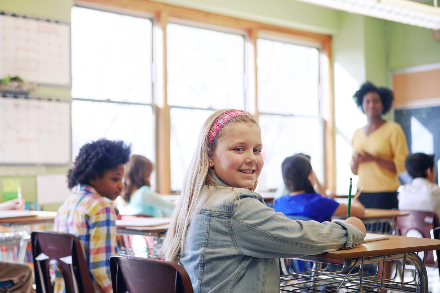 Autistic student smiling at the camera while sitting at a desk in a classroom.