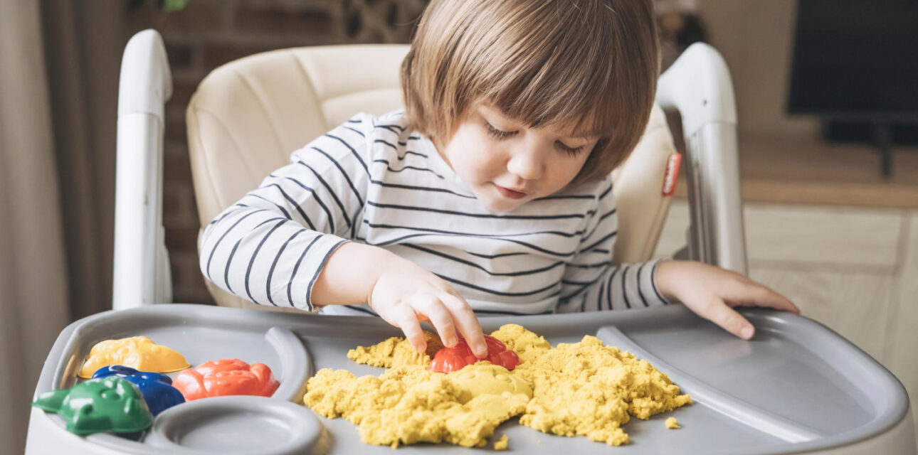 Child with autism playing with sensory sand in a high chair during in-home ABA therapy.