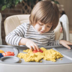 Child with autism playing with sensory sand in a high chair during in-home ABA therapy.