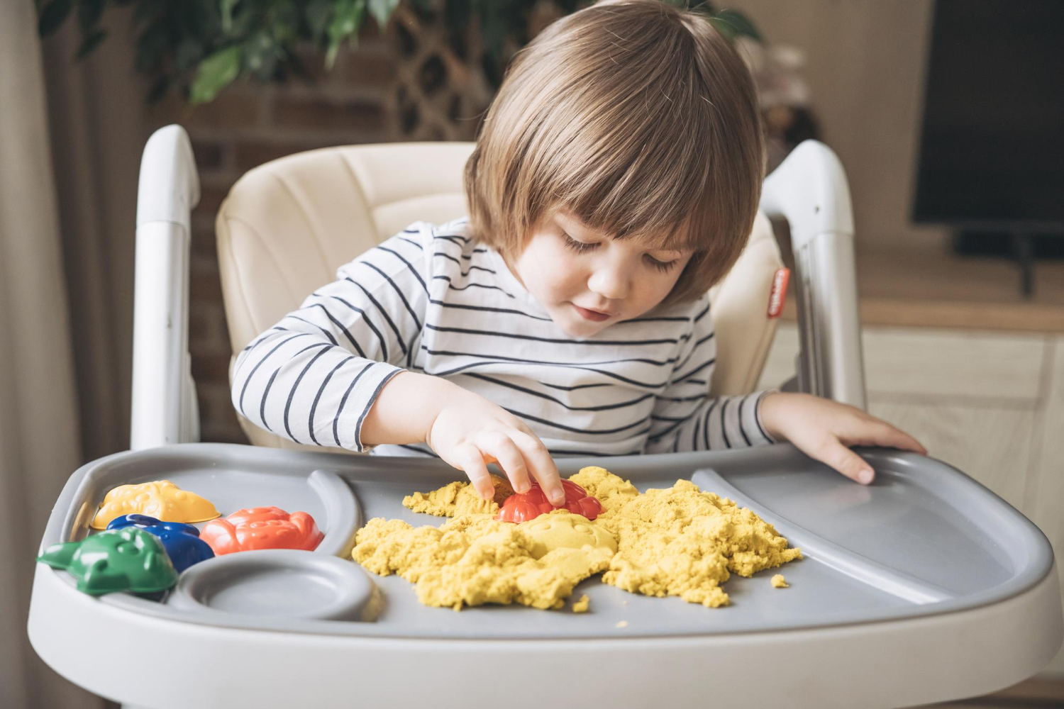 Child with autism playing with sensory sand in a high chair during in-home ABA therapy.