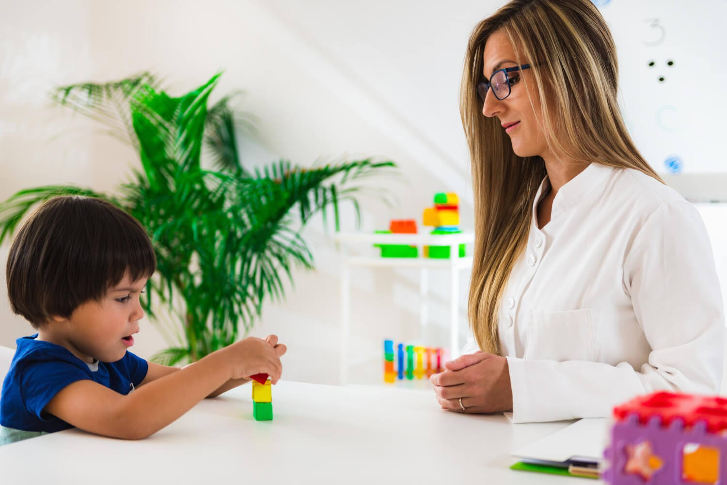 Child practicing skills with an ABA therapist using colorful blocks.