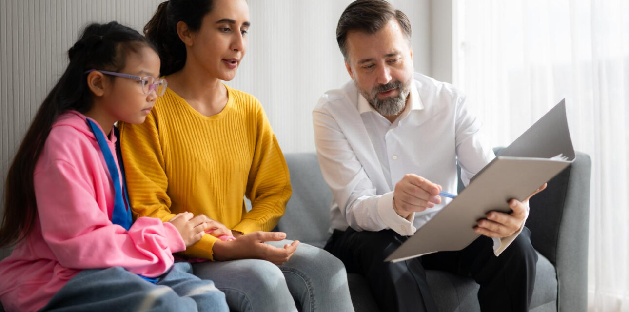 A BCBA reviews documents with a parent and child during an ABA therapy consultation.