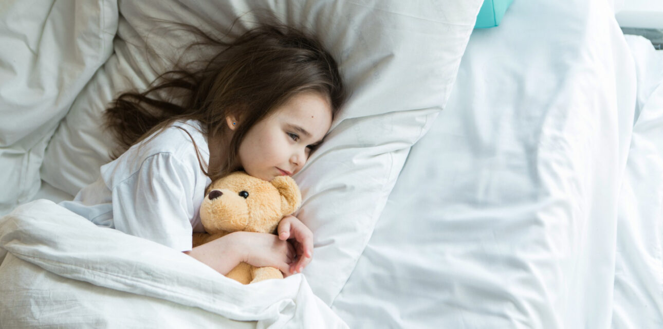 Autistic child lying in bed with a teddy bear at bedtime.
