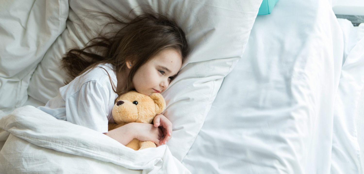 Autistic child lying in bed with a teddy bear at bedtime.