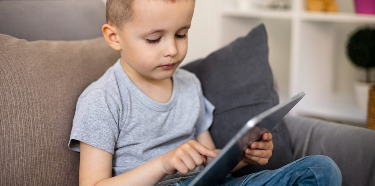 Young boy with autism sitting on a couch and using a tablet.