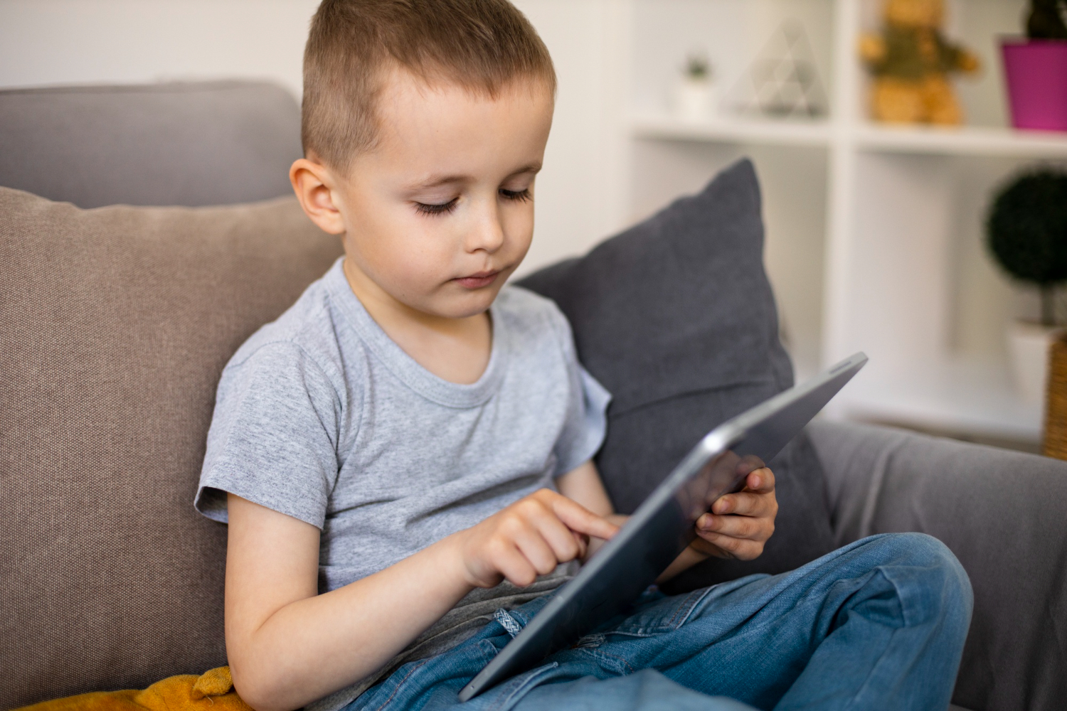 Young boy with autism sitting on a couch and using a tablet.