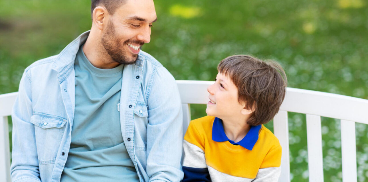 Father and autistic child smiling together on a park bench.