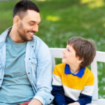Father and autistic child smiling together on a park bench.