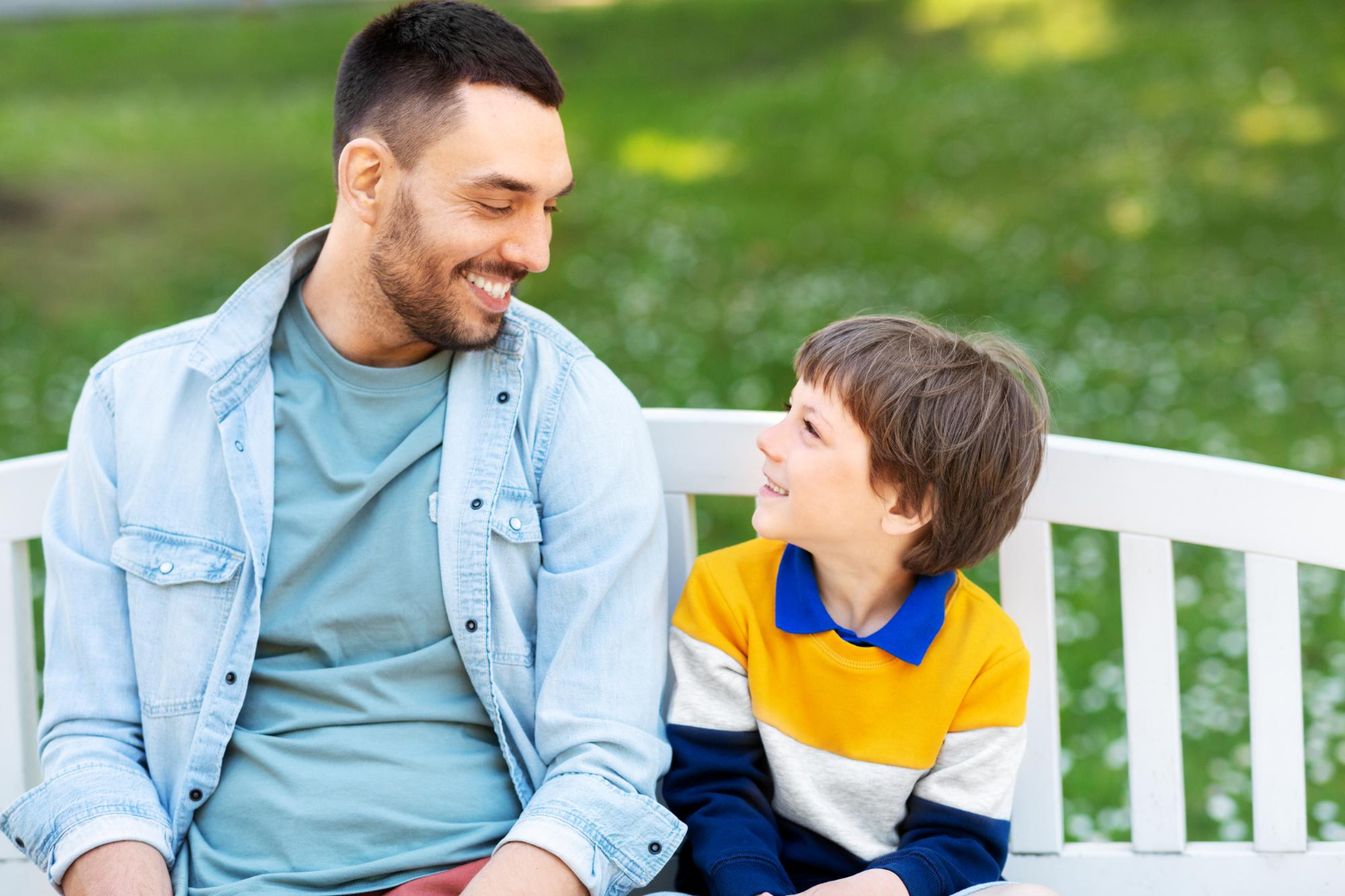 Father and autistic child smiling together on a park bench.