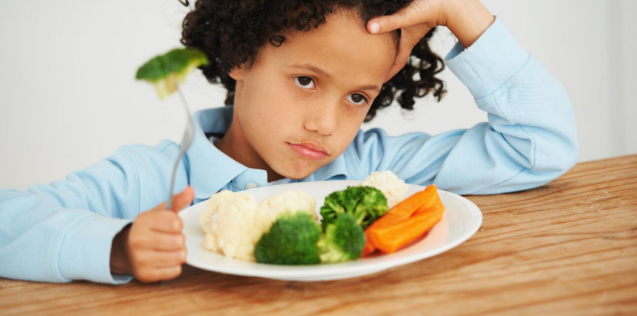 Autistic child looking unhappy at a plate of vegetables during mealtime.