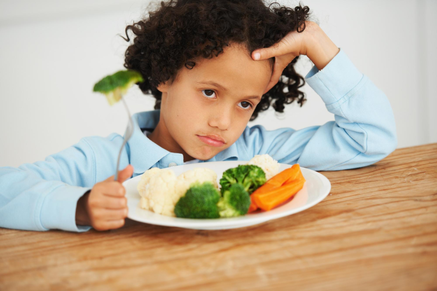 Autistic child looking unhappy at a plate of vegetables during mealtime.