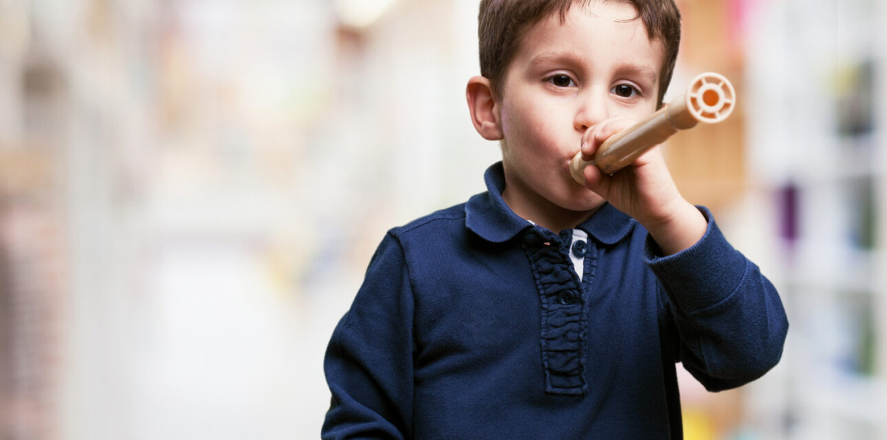 Young boy holding a toy tube to his mouth indoors.
