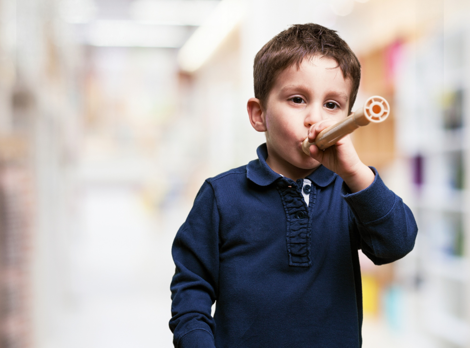 Young boy holding a toy tube to his mouth indoors.