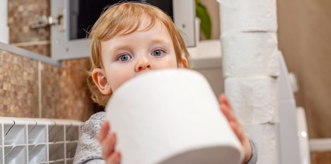 Young child holding a roll of toilet paper in a bathroom.