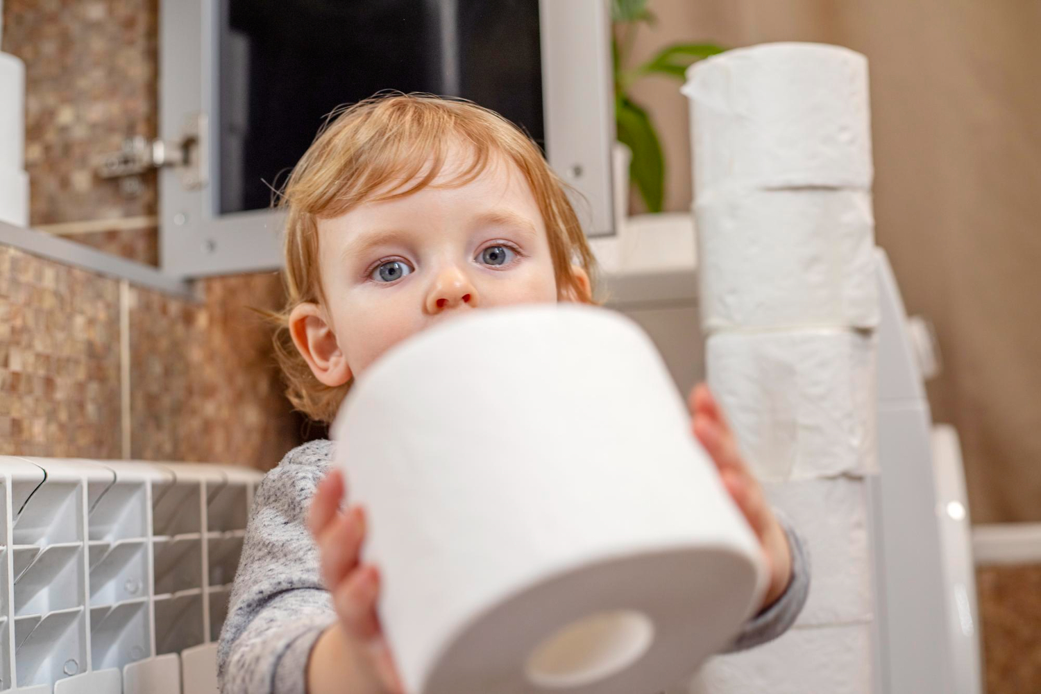 Young child holding a roll of toilet paper in a bathroom.
