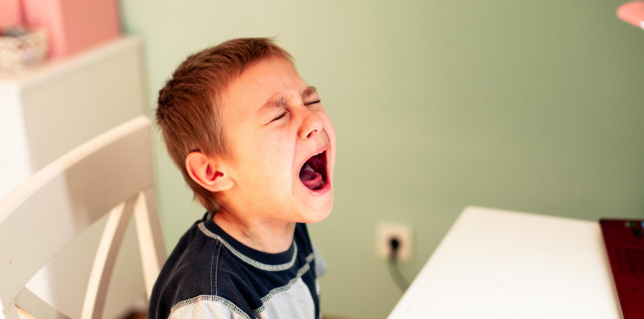 Autistic child crying while sitting at a table.